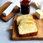 An image of a freshly baked loaf of cassava bread, it has a golden crust and a fluffy inside. The bread is sliced and served on a wooden cutting board and there is butter or jam on top of it