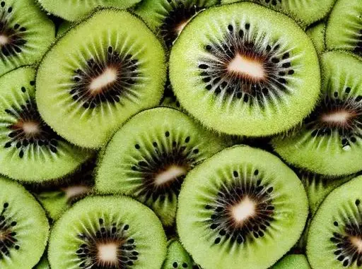 An image of a ripe kiwi, sliced in half to reveal its vibrant green flesh and black seeds. The fuzzy brown exterior of the fruit contrasts with the soft, juicy texture of the interior. The kiwi is placed on a white surface, surrounded by other colorful fruits such as strawberries and blueberries, making for a visually stunning composition